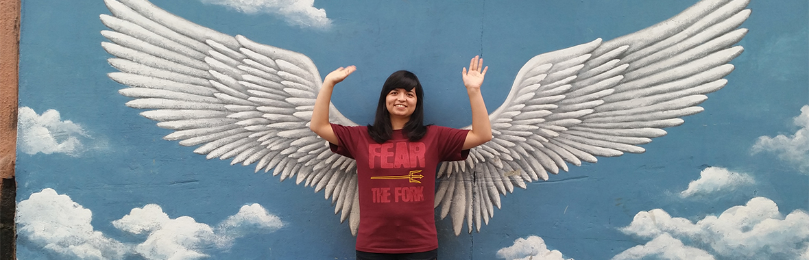 Person holding their hands up standing in front of a wall with wings painted on it
